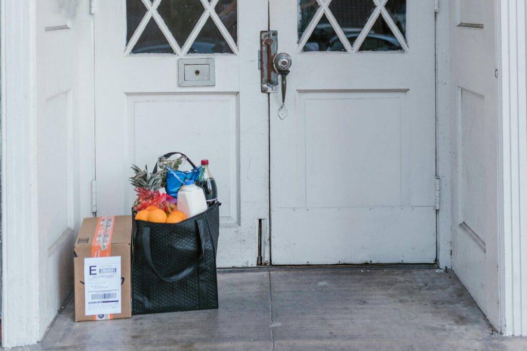 A personal shopper unloading grocery bags from a car in front of a suburban home. The image conveys small business service, approachability, and everyday convenience.