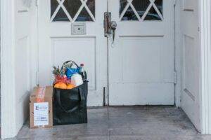 A personal shopper unloading grocery bags from a car in front of a suburban home. The image conveys small business service, approachability, and everyday convenience.