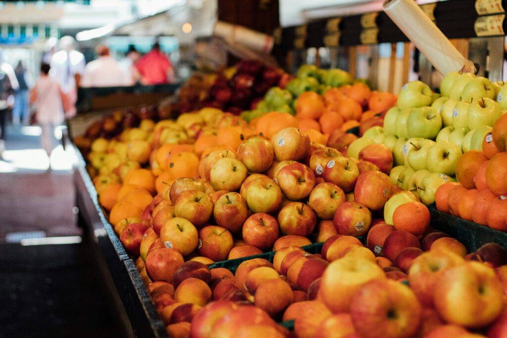 A fall harvest mix of fresh apples, pears, grapes, squash, and leafy greens arranged on a wooden table. The image conveys early autumn freshness and farm-to-table shopping.
