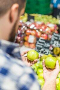 A personal shopper examining avocados in the produce aisle, checking for ripeness. The image conveys attention to detail, freshness, and quality shopping.