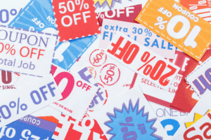 A close-up of a personal shopper’s hand checking a grocery list with notes about substitutions and clipped coupons beside a cart. The image suggests attention to detail and customized service.