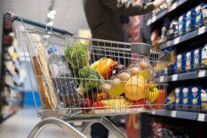 A personal shopper checking produce in a grocery store, inspecting a piece of fruit for ripeness while holding a detailed shopping list. The image conveys care, quality, and attention to detail.
